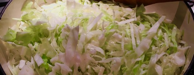 white and green sliced cabbage in a white enamel pot on stove with wooden spoon ©gillstannard naturopath