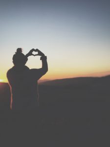 silhouette of woman holding hands in heart shape against a sunset 