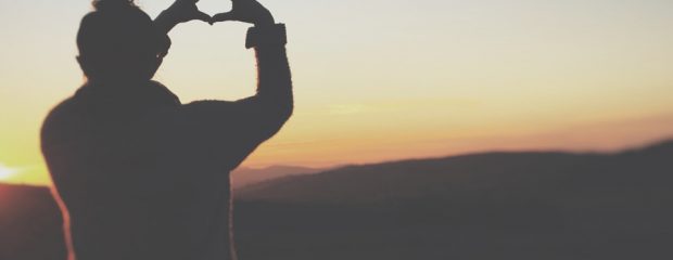 silhouette of woman holding hands in heart shape against a sunset