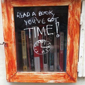 street library orange painted wood around a glass window with read a book you've got time" written in white texta