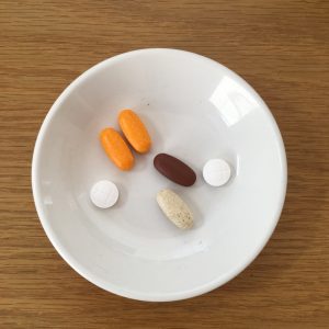 a small white plate holding 2 orange, 3 white and one brown tablet