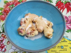 large knob of ginger covered with salt in a blue bowl with on a multicoloured tea towel