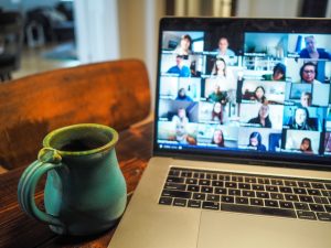 macbook open on desk with multiple faces on zoom call green mug to left of computer