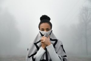 woman of colour with dark hair in a bun at top of head holds gray and black geometric striped scarf of pbdy and lower face background white mist it looks cold