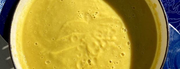 large blue enamel pot full of yellow soup on blue background