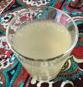 glass of off white liquid with bubbles on a brown, teal and white backgrond