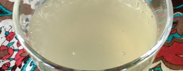 glass of off white liquid with bubbles on a brown, teal and white backgrond