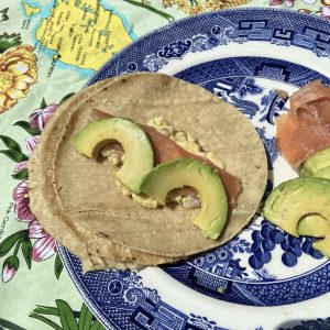 soft tortillas with scrambled eggs, smoked salmon and half moons of avocadom on a blue willow pattern plate sitting on a map of New Zealand