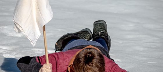 a person dressed in red and black lies face down in the snow planting a white flag on a stick