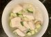 whote bowl on dark granite backgrou. In bowl is a clear soup with chunks of silken tofu and slices of ginger and zuccini, on fine rice noodles