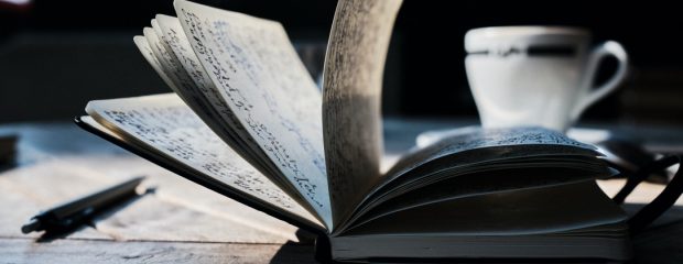 pages of open journal and white and blue tea cup