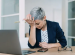 Middle aged woman with short grey hair sits at desk and open laptop with head in her hand looking exhausted is she anaemic?
