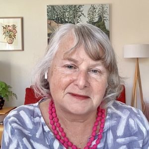 middle aged white woman with grey blonde hair wearing blue and white shirt and double strand of red beads