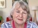 middle aged white woman with grey blonde hair wearing blue and white shirt and double strand of red beads